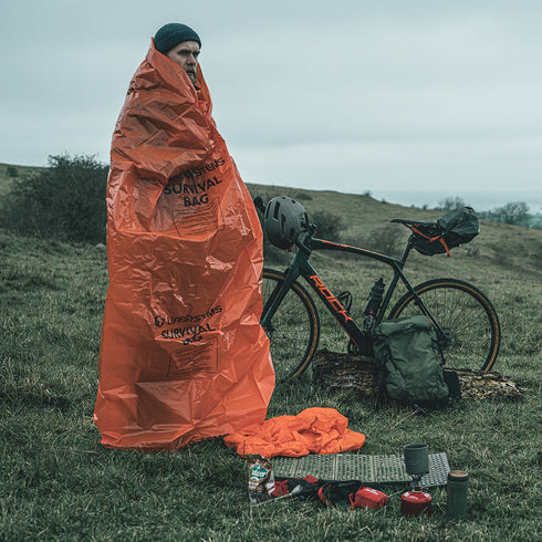 Cyclist wrapped in the Lifesystems Survival Bag beside a bike