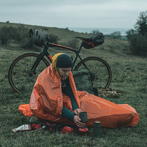Cyclist resting in the Lifesystems Survival Bag on a hillside