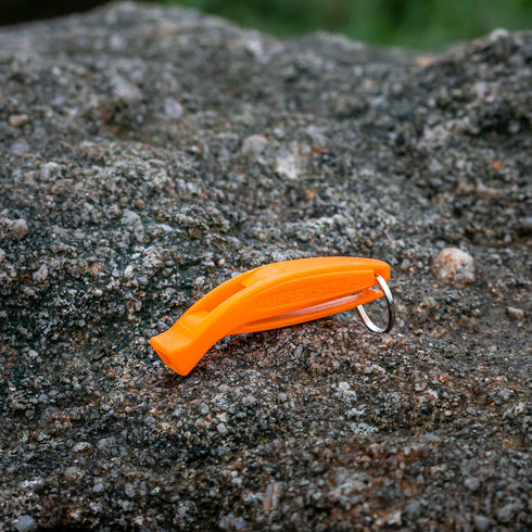 Lifesystems Echo Whistle, orange, lying on a gravel path