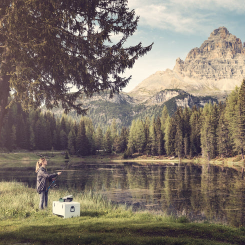 Woman fishing at a mountain lake with a Dometic Cool-Ice 42 in Stone