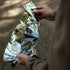Hiker wrapped in a Coghlan's silver emergency blanket in a forest