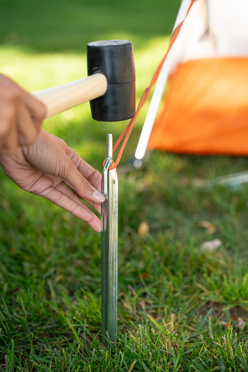 Camper driving a steel tent stake into the ground at a campsite